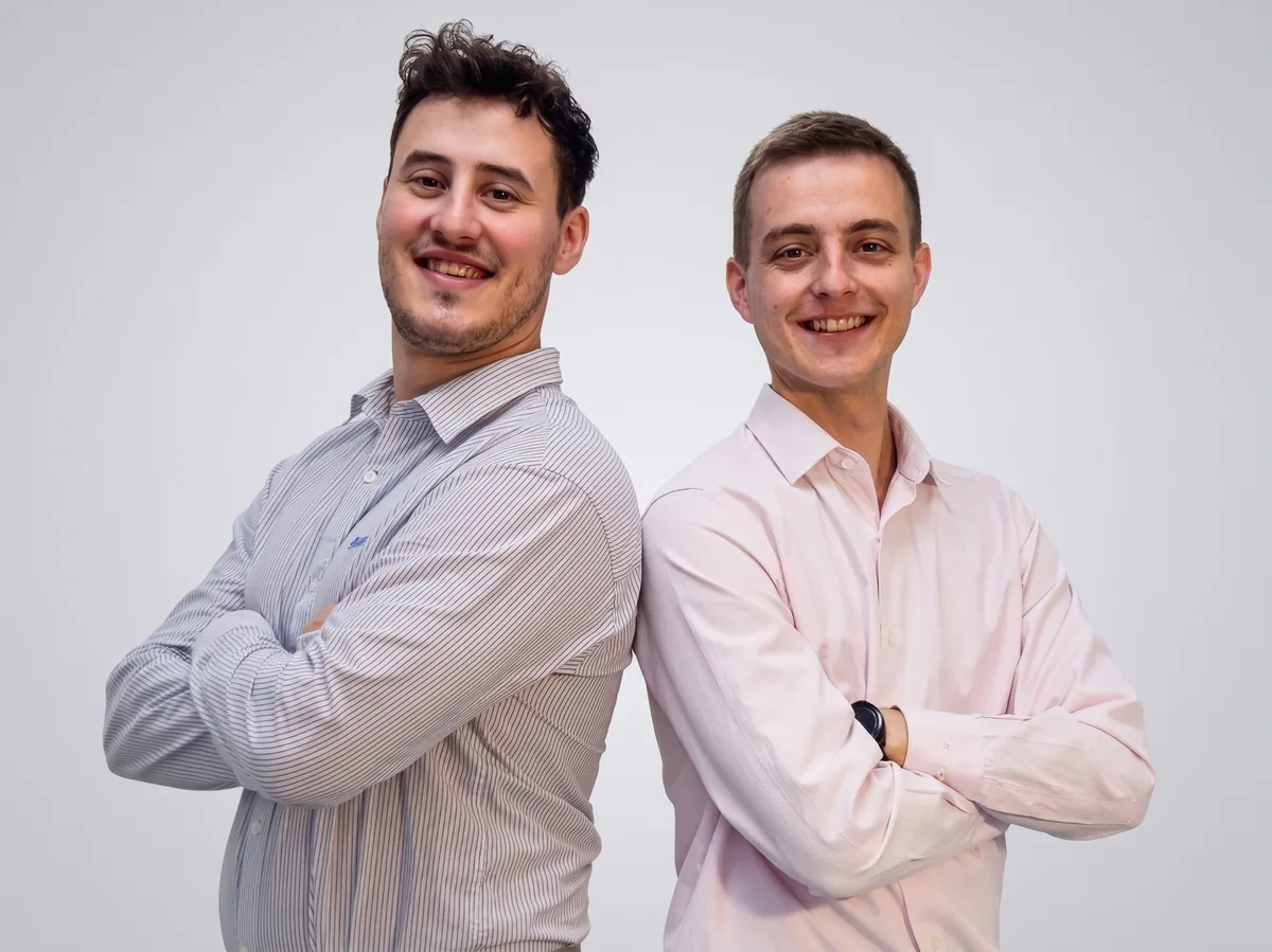 Nacho y Patricio, los dos socios fundadores de Siadon, sonrientes, espalda con espalda y de brazos cruzados en la oficina; atrás, una pantalla con el logo de Siadon.